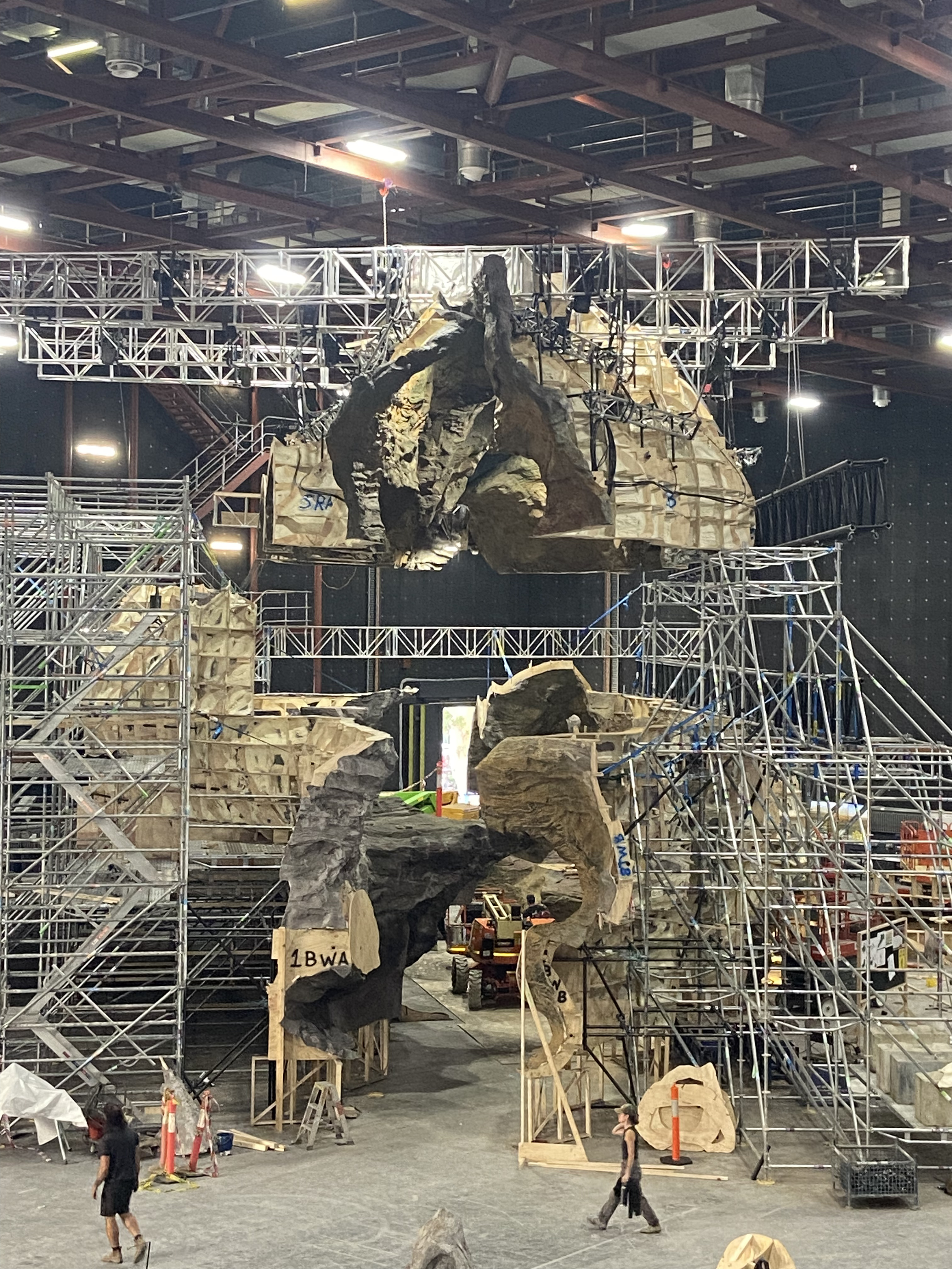 Front view of the cave construction showing the suspended modular roof above the scaffold and scenic structure.