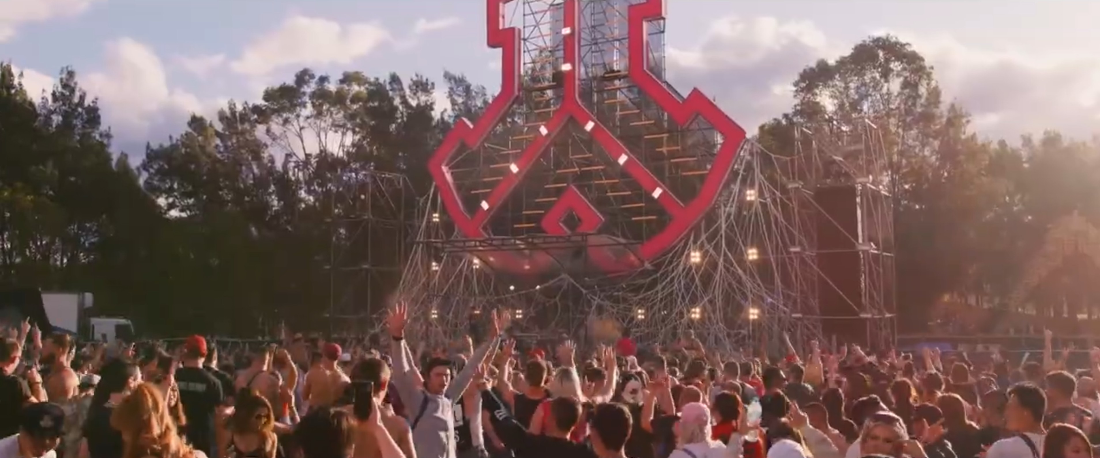 Crowd facing a towering Defqon.1 logo stage built in scaffold and scenic mesh.